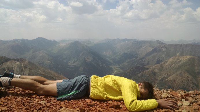 An exhausted hiker laying facedown on the summit of Redcloud Peak