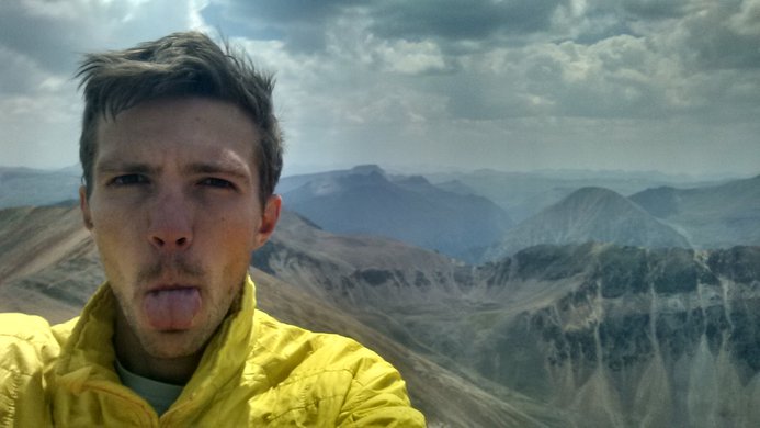A defiant hiker sticking his tongue out on the summit of Redcloud Peak with Sunshine Peak in the background