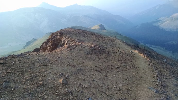 The trail down Wetterhorn Peak's southeast ridge curves through yellow soil
