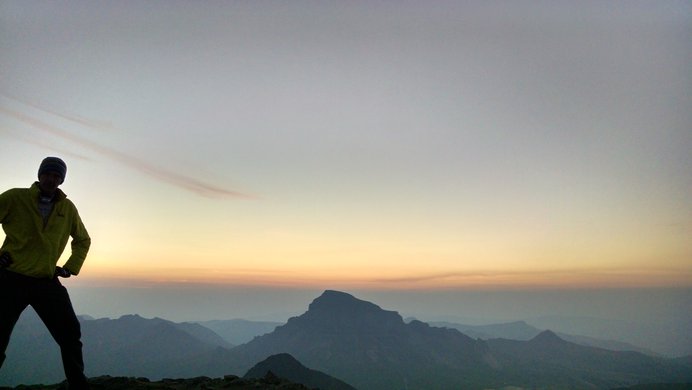 A hiker's silhouette with the glow of sunrise behind Uncompahgre Peak beyond